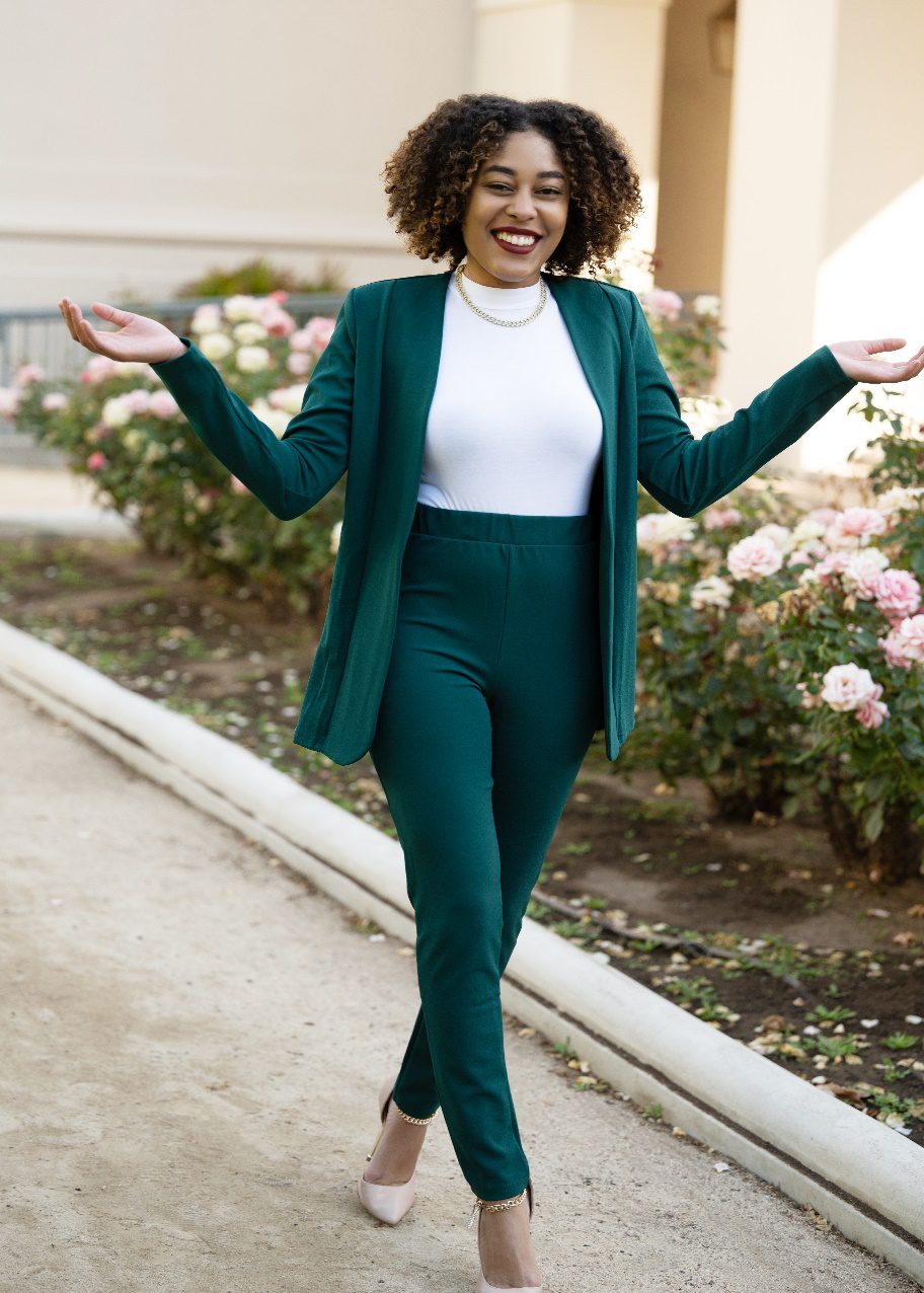 A Woman in a Green Suit Walking on a Path With Pink Flowers on the Side